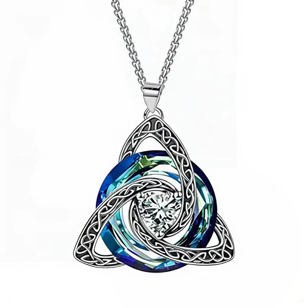 A silver Celtic knot triquetra pendant necklace featuring a central clear crystal and layered blue and green iridescent spiral inlay, suspended from a silver chain against a white background.