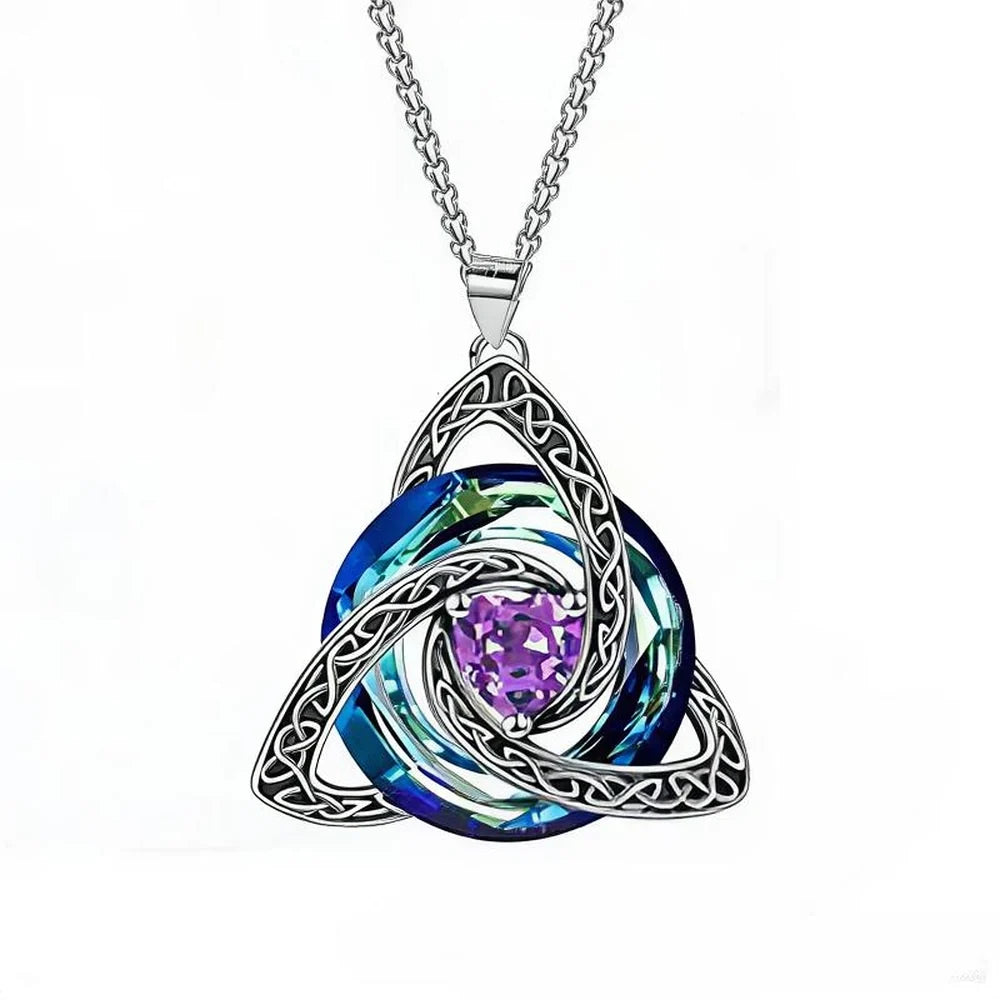 A silver Celtic knot triquetra pendant necklace featuring a central purple heart-shaped crystal surrounded by layered blue and green iridescent swirls, suspended from a silver chain on a white background.