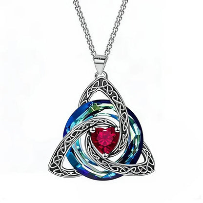 A silver Celtic triquetra knot pendant necklace featuring a central faceted red heart gemstone and layered blue and green iridescent circular elements, suspended from a silver chain on a white background.