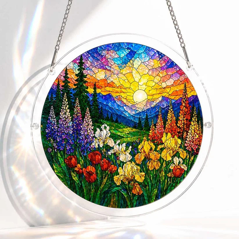 A round acrylic suncatcher showing a stained glass sunlit wildflower valley with iris tulips pine trees and distant mountains
