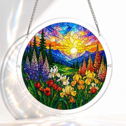 A round acrylic suncatcher showing a stained glass sunlit wildflower valley with iris tulips pine trees and distant mountains