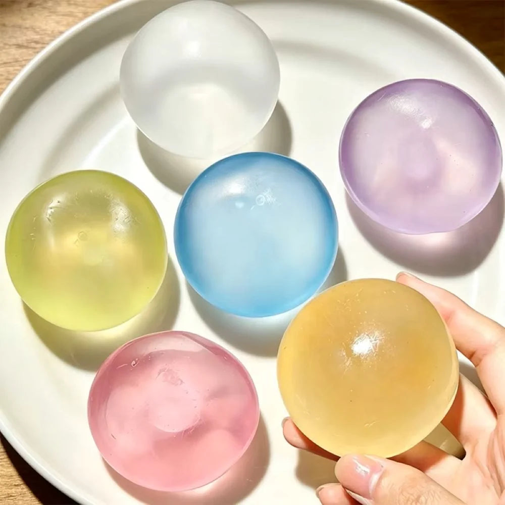 Six translucent coconut oil ball in pastel colors are arranged on a white plate, with a hand holding one amber-colored sphere in the foreground.