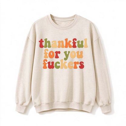 A cream crew neck sweatshirt printed with three lines of retro multicolor Thanksgiving lettering on a white background