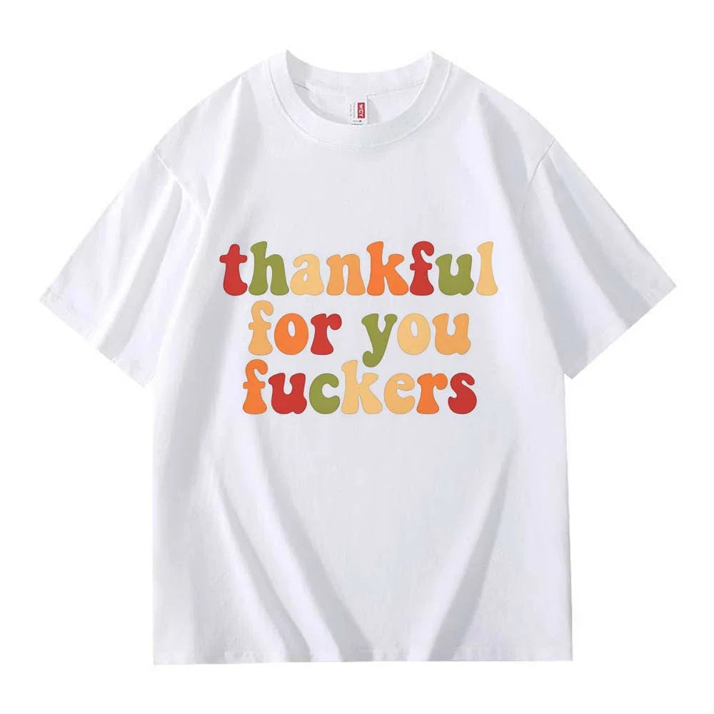 A white crew neck T-shirt with three lines of retro multicolor Thanksgiving lettering laid flat on a white background