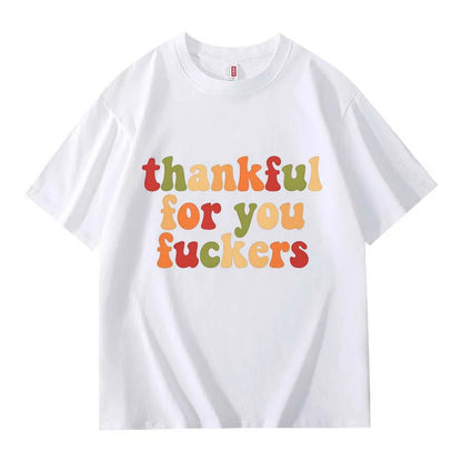 A white crew neck T-shirt with three lines of retro multicolor Thanksgiving lettering laid flat on a white background
