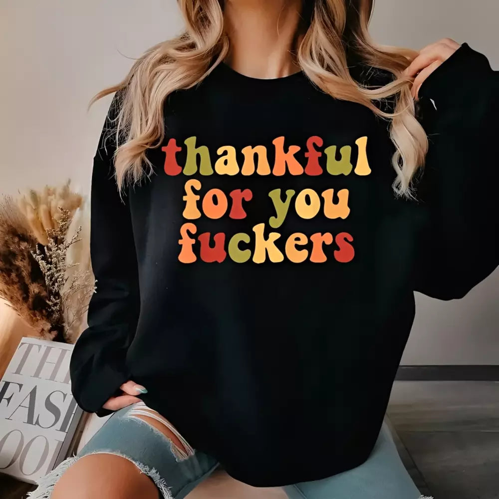 A blonde woman wearing a black sweatshirt printed with vintage colorful Thanksgiving text posing with torn denim shorts