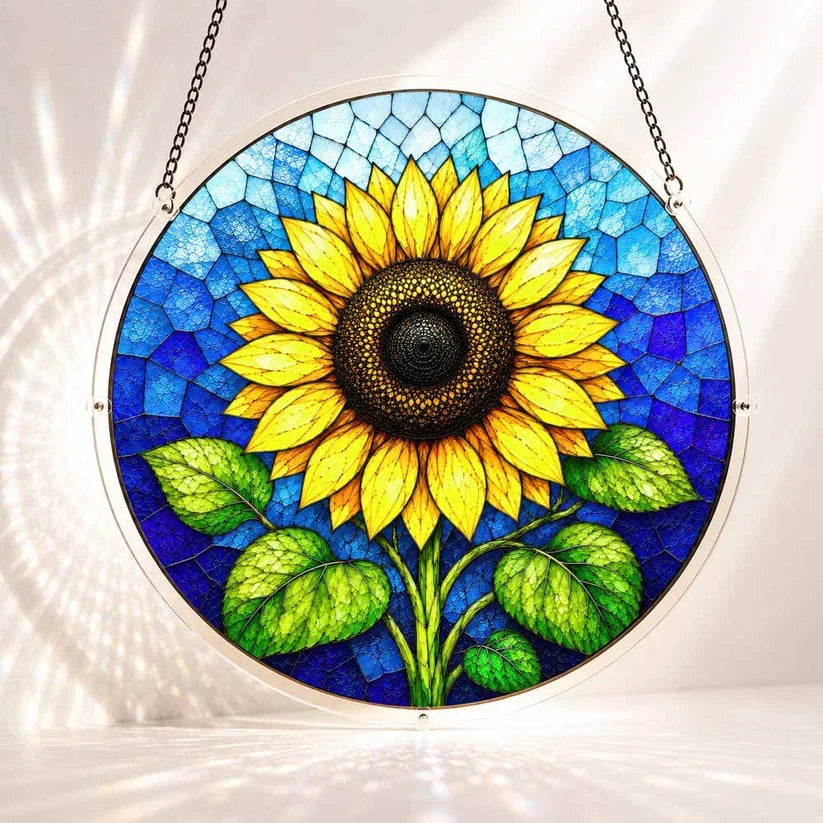A round acrylic suncatcher featuring a large golden sunflower with green leaves against a blue stained glass background