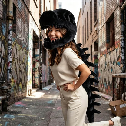 A woman wearing a black dinosaur skull and spine costume stands in a graffiti-covered alleyway, smiling and posing with one leg extended.