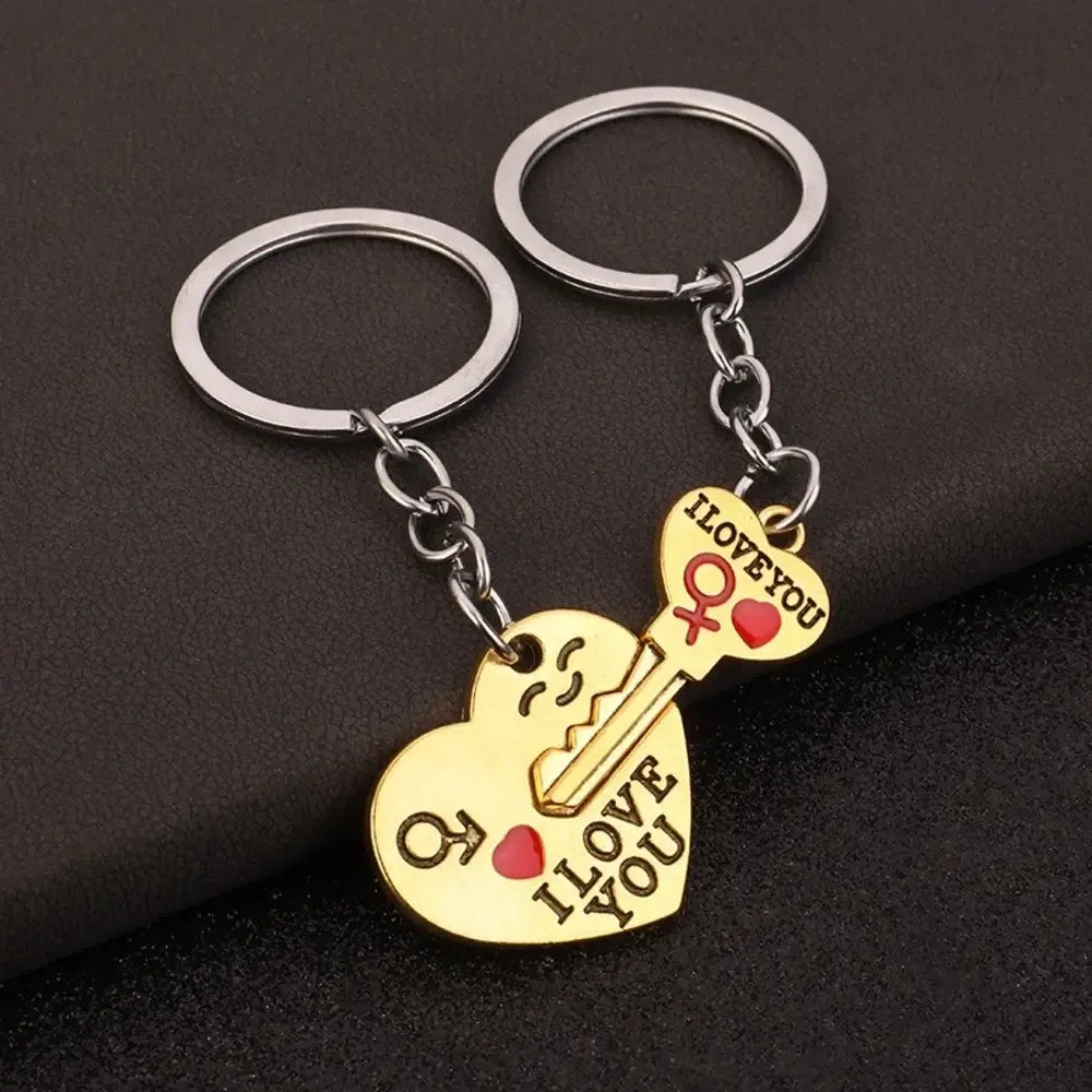 Two gold heart-shaped keychains with silver key rings, one shaped like a smiling face and the other like a key, both engraved with 'I LOVE YOU' and a small red heart, displayed on a dark textured background.