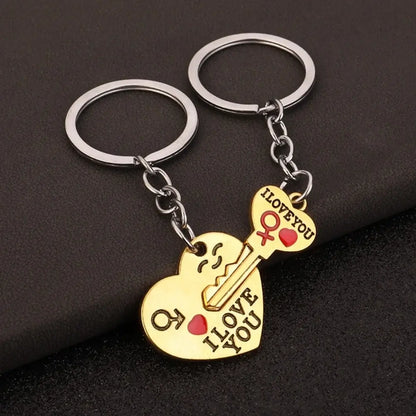 Two gold heart-shaped keychains with silver key rings, one shaped like a smiling face and the other like a key, both engraved with 'I LOVE YOU' and a small red heart, displayed on a dark textured background.