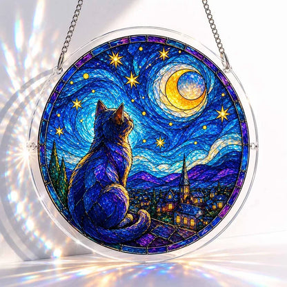 A round acrylic suncatcher of a blue cat sitting under a crescent moon and stars overlooking a lit village at night