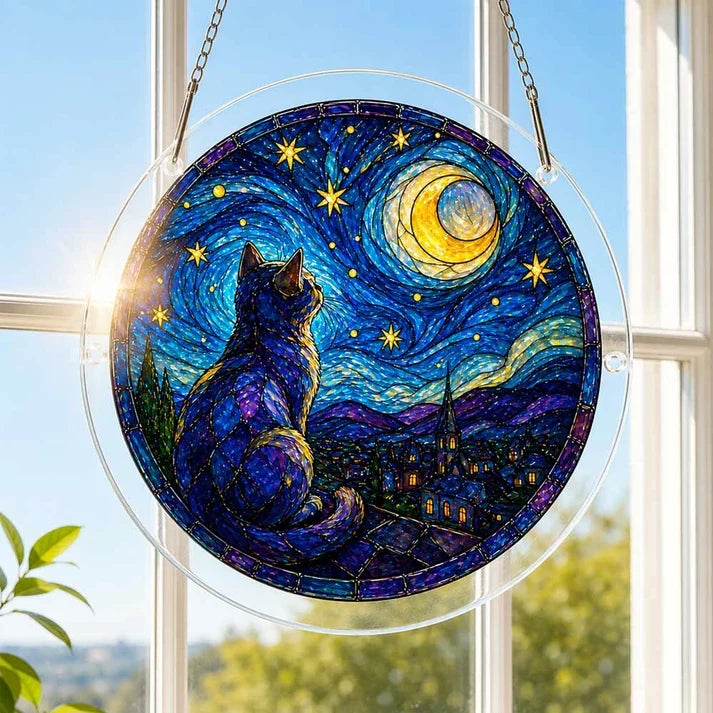 A round acrylic suncatcher with a purple cat gazing at a swirling starry sky hanging from a chain in front of a bright white window