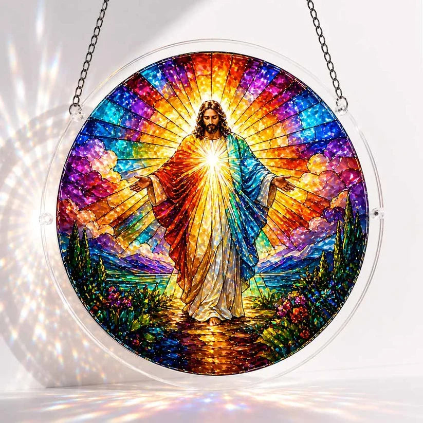 A round acrylic suncatcher depicting a radiant Jesus figure with open arms surrounded by rainbow light clouds and mountains