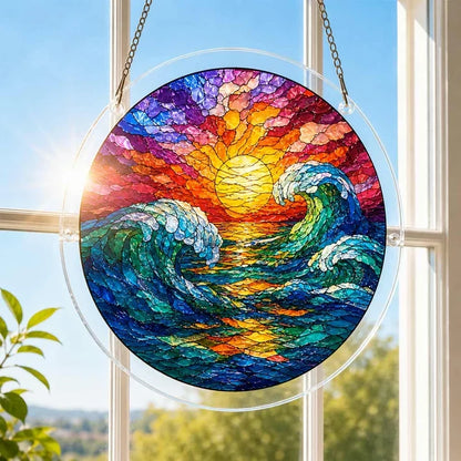A round acrylic suncatcher with curling turquoise waves beneath a golden sun hanging from a chain in front of a bright white window