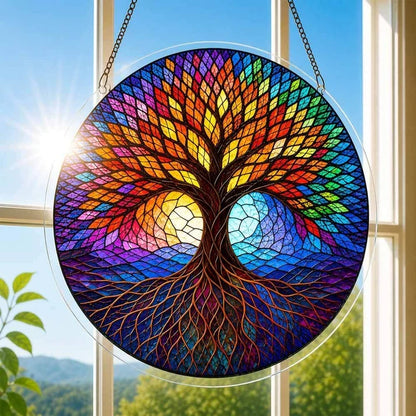 A round acrylic suncatcher with a rainbow tree of life flanked by sun and moon hanging from a chain in front of a bright white window