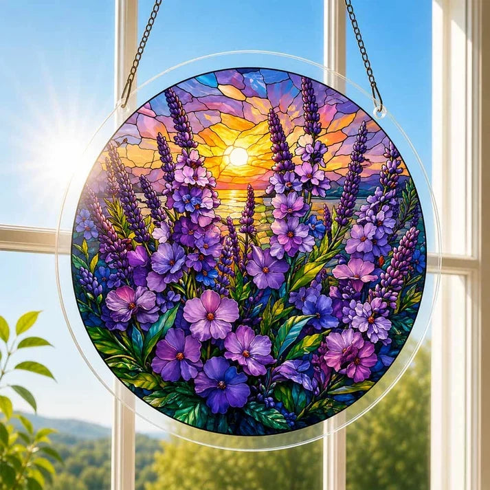 A round acrylic suncatcher filled with purple wildflowers beneath a glowing sunset hanging from a chain in front of a bright white window
