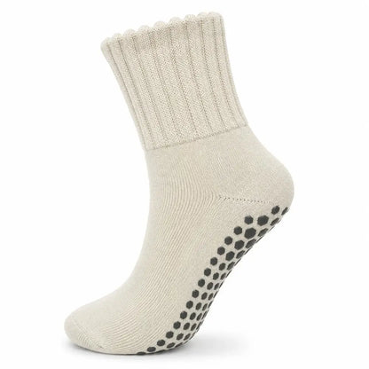 A single ankle-length knit sock in a warm off-white or cream color, featuring a scalloped ribbed cuff and black grip dots on the sole, shown against a plain white background.