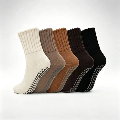 Six ankle socks arranged in a row on a light gray background, showing different color options: off-white, taupe, camel, very dark brown, charcoal, and black. Each sock has a ribbed cuff and a grip pad with raised dots on the sole.