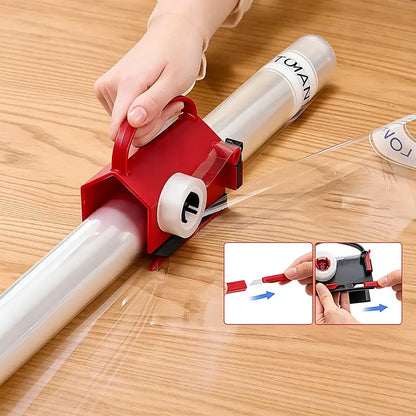A red plastic roll of clear film dispenser being used on a wooden table, with a hand guiding the clear film. Two small inset diagrams at the bottom show additional usage angles.